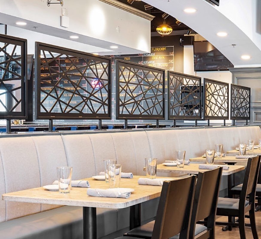 Custom framed geometric architectural metal privacy screens installed as booth dividers in a modern luxury commercial restaurant interior.